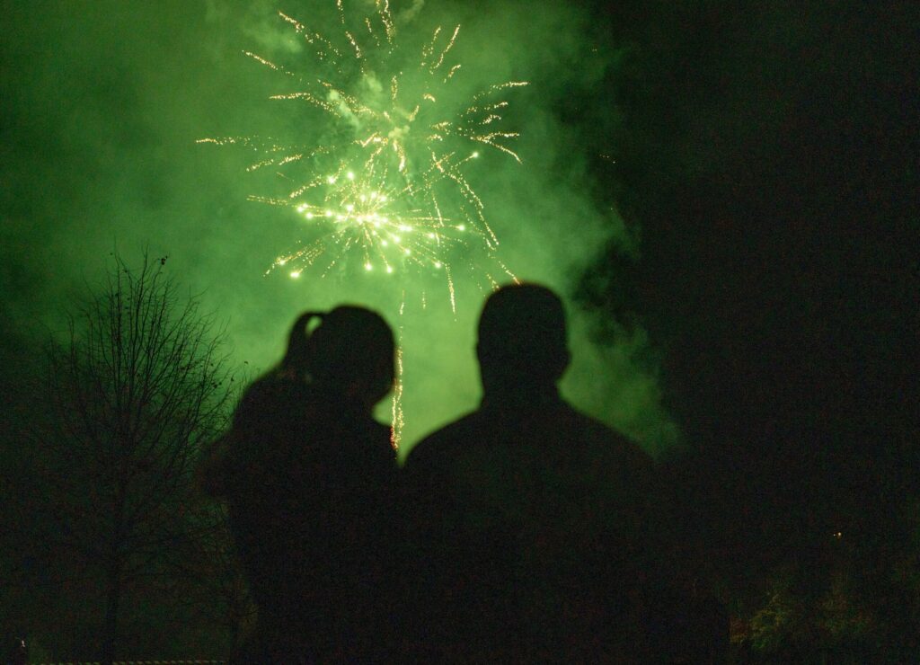 Zwei Personen schauen sich das Feuerwerk bei Bremer Lichter an, im Nachthimmel leuchtende Funken.